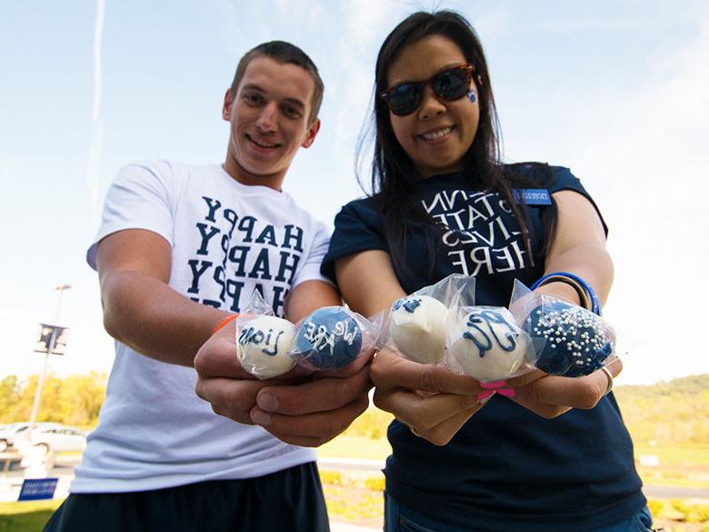 penn state alumni holding PSU-themed cake pops and smiling at the camera in their penn state gear