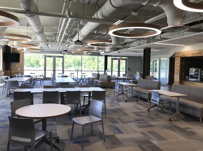 a large room with an exposed ceiling, a wall of windows, and multiple round tables and booths.