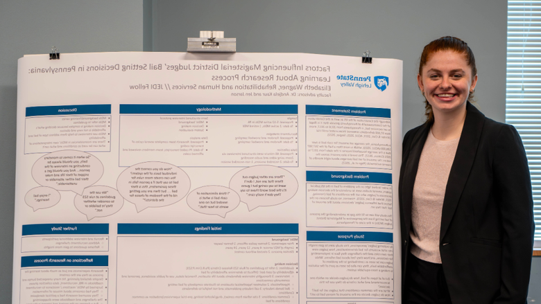 A student smiling next to a research poster